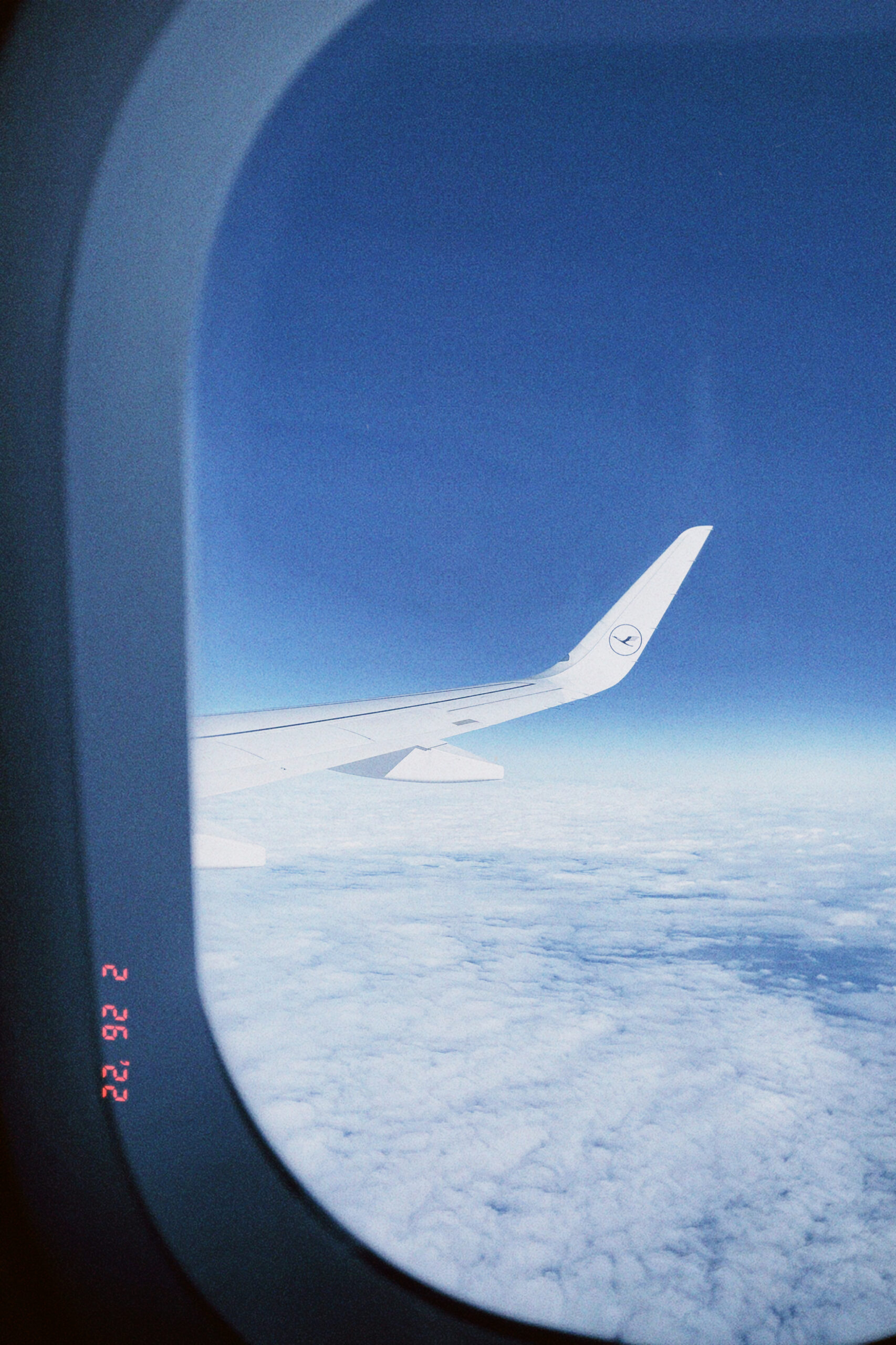 a plane wing through the window of a plane flying over clouds